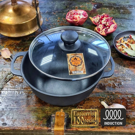 Black cast iron pot with lid on a rustic wooden surface with pomegranate and other items.