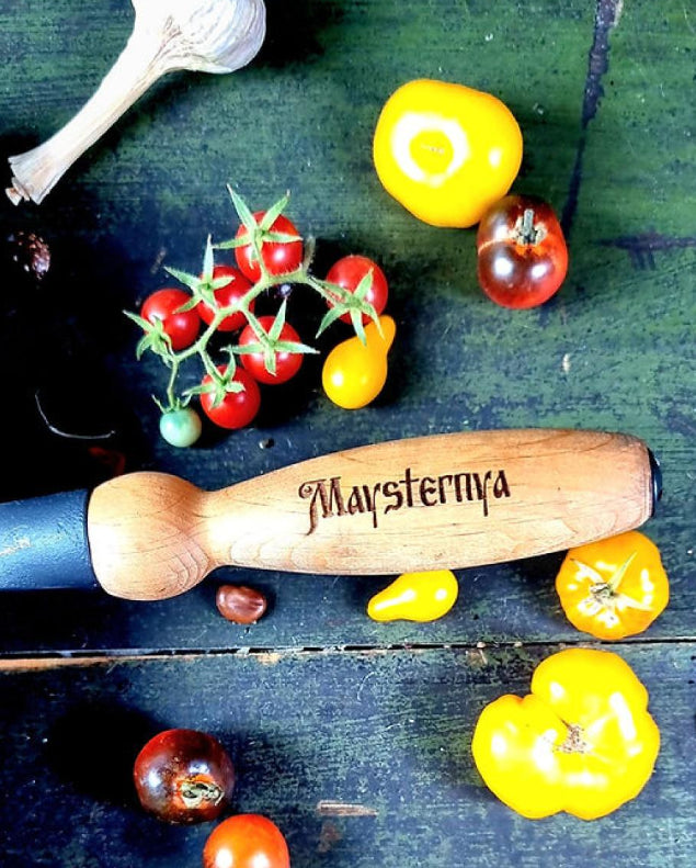 Wooden rolling pin with 'Maysternya' branding on a dark surface with vegetables.