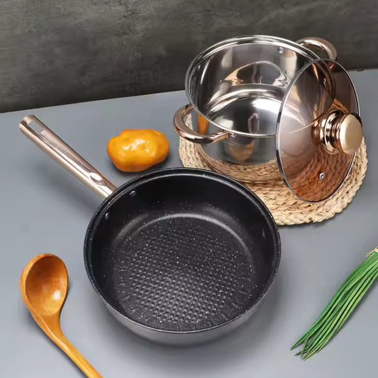 Black frying pan with a wooden spoon and green herbs on a gray surface