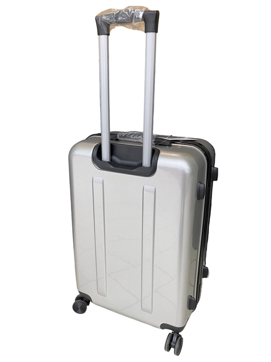 Silver suitcase with black wheels on a tiled floor with a black curtain and cardboard box in the background.