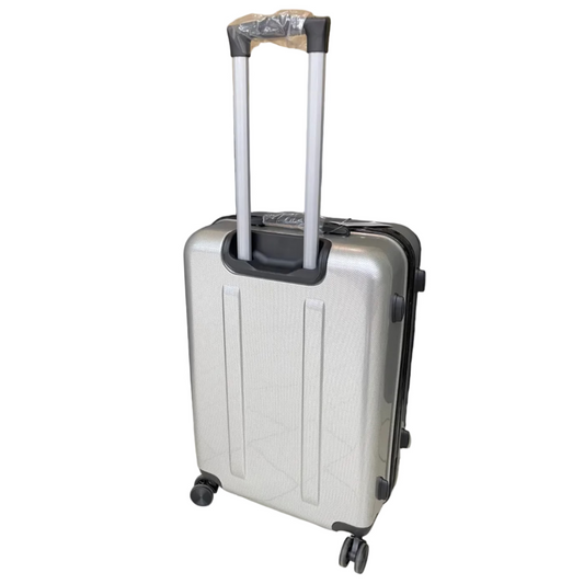 Silver suitcase with black wheels on a tiled floor with a black curtain and cardboard box in the background.
