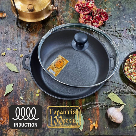 Black frying pan with lid on a rustic wooden surface with pomegranate, leaves, and garlic.