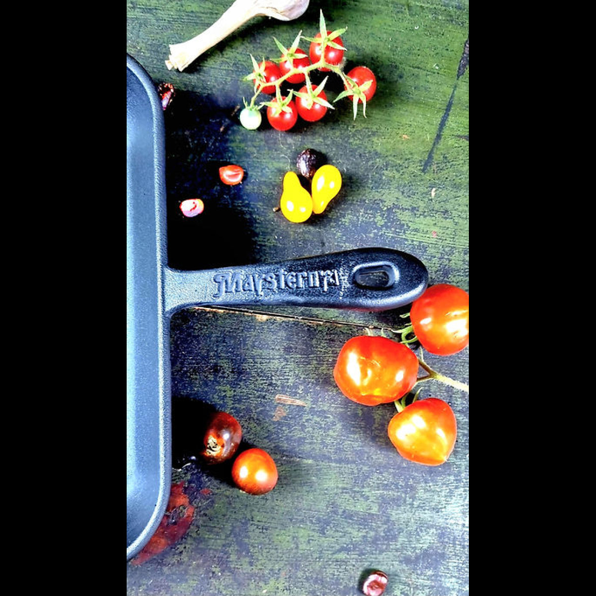 Black cast iron frying pan with vegetables on a green surface