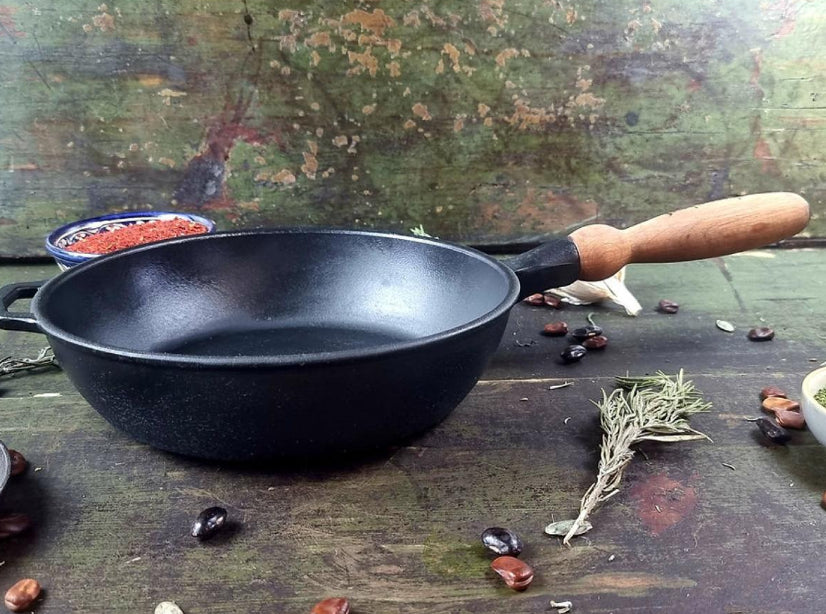 Black cast iron frying pan with wooden handle on a rustic surface with ingredients