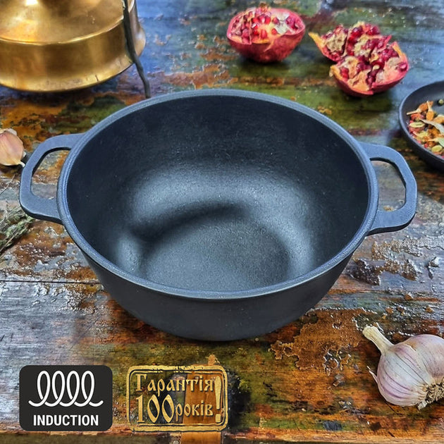 Black cast iron pot on a rustic wooden surface with pomegranates and garlic.