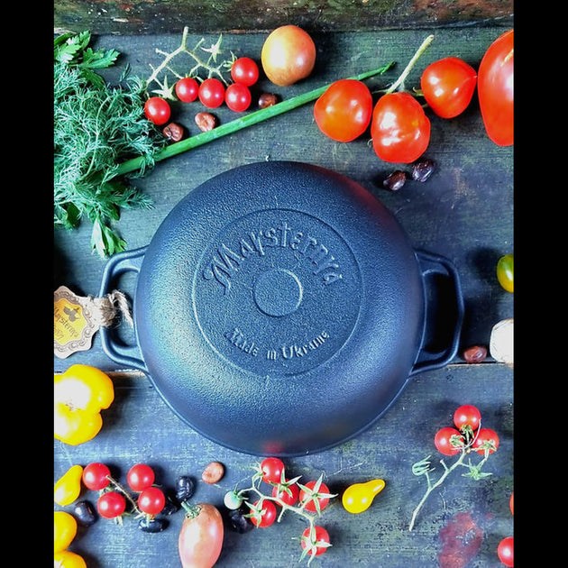 Blue cast iron skillet with 'Vallasterra' branding on a wooden surface with vegetables.