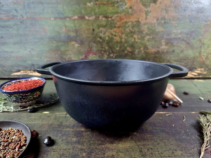 Black cast iron pot on a rustic wooden surface with spices and herbs.