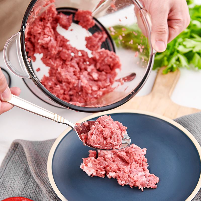 Minced meat being transferred from a grinder to a blue plate using a spoon.