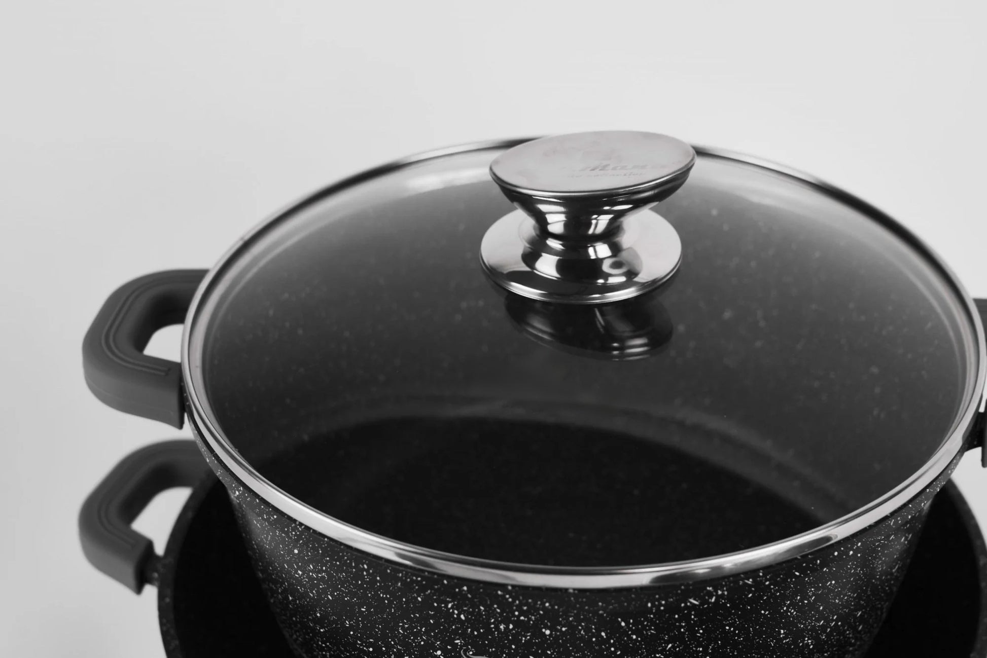 Black speckled cookware with a glass lid on a light gray background