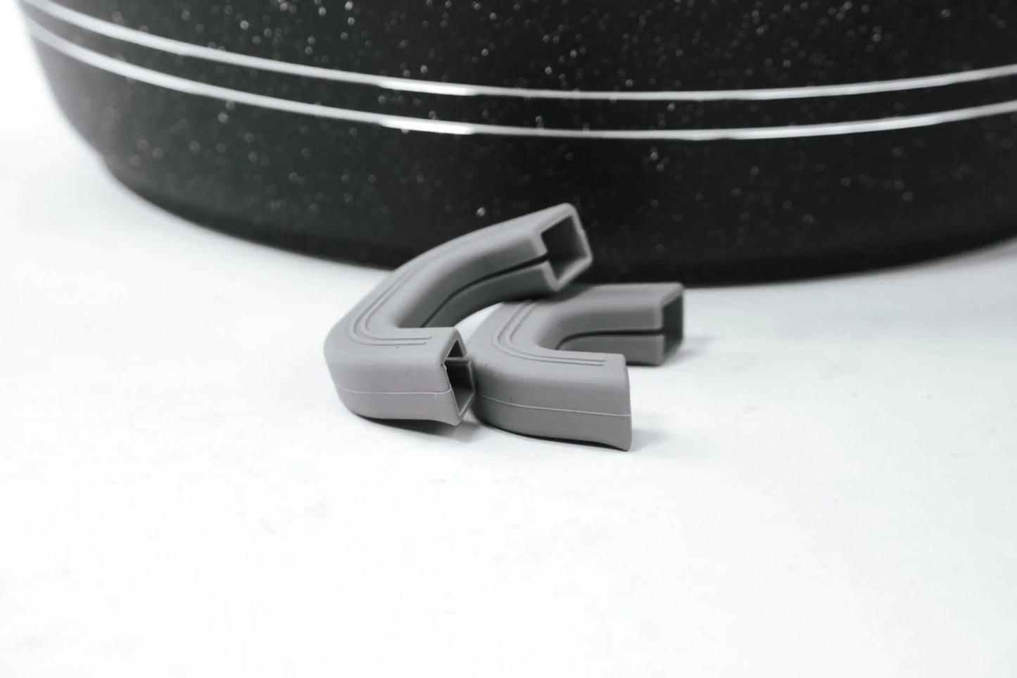 Gray silicone clip on a white background with a black speckled object in the background