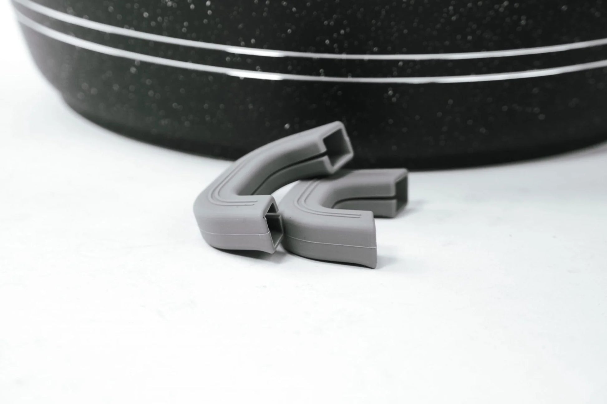 Gray plastic clip on a white background with a black speckled object in the background