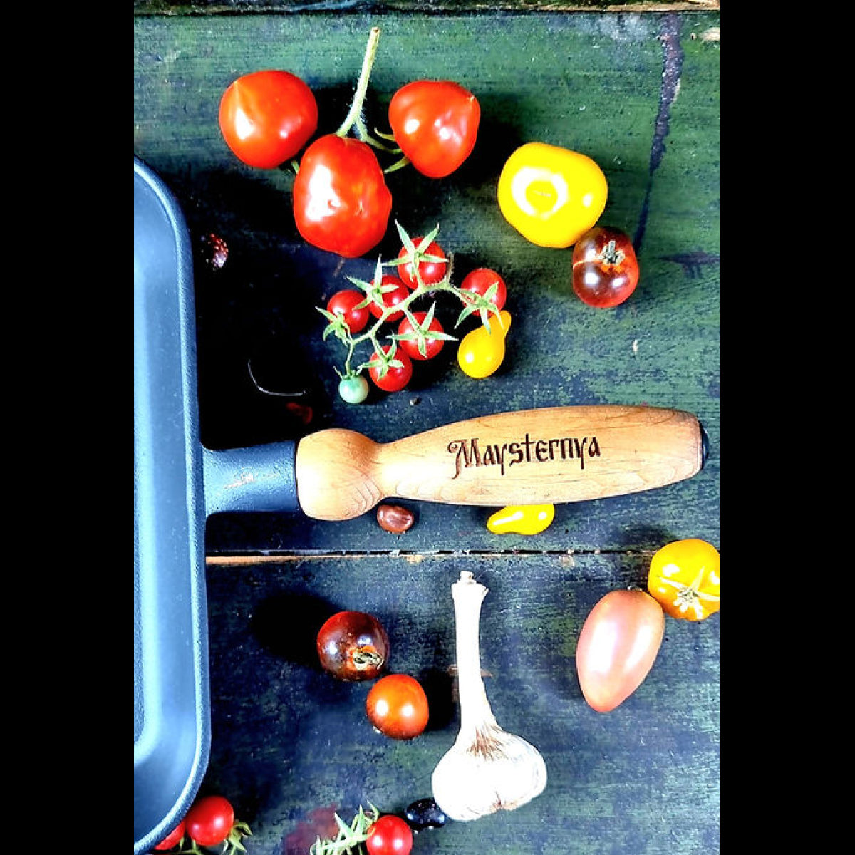 Tomatoes, garlic, and a wooden tool on a green surface with 'Maysternya' branding.