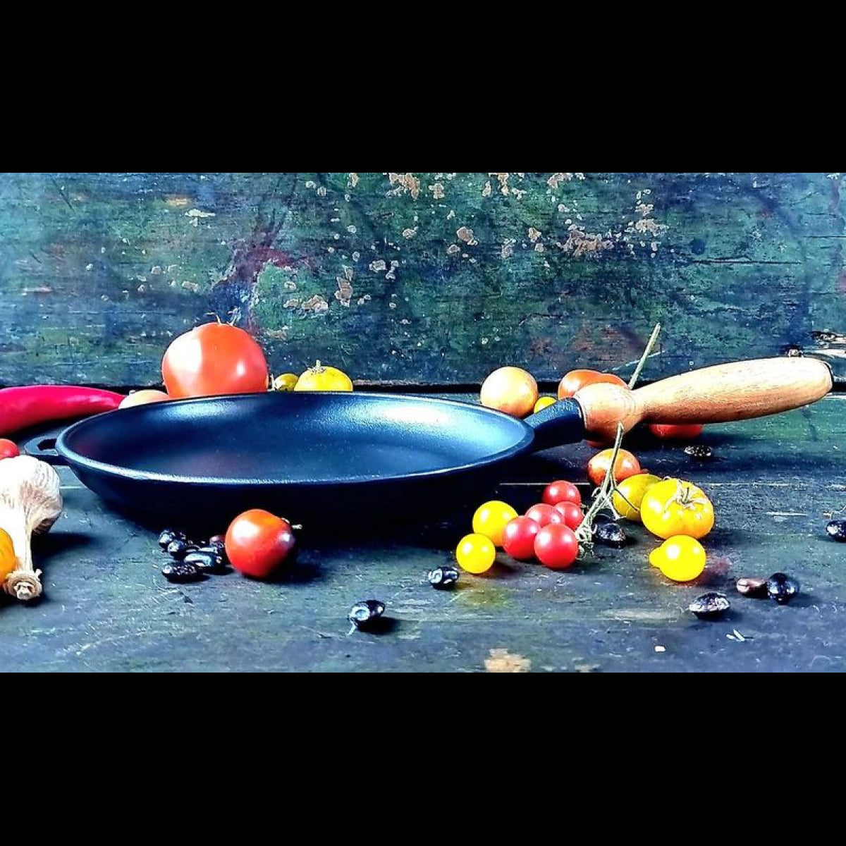 Black cast iron pancake pan on a dark surface with vegetables around
