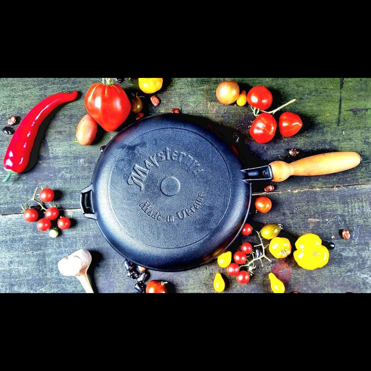 Black cast iron pancake pan with wooden handle on a wooden surface with vegetables