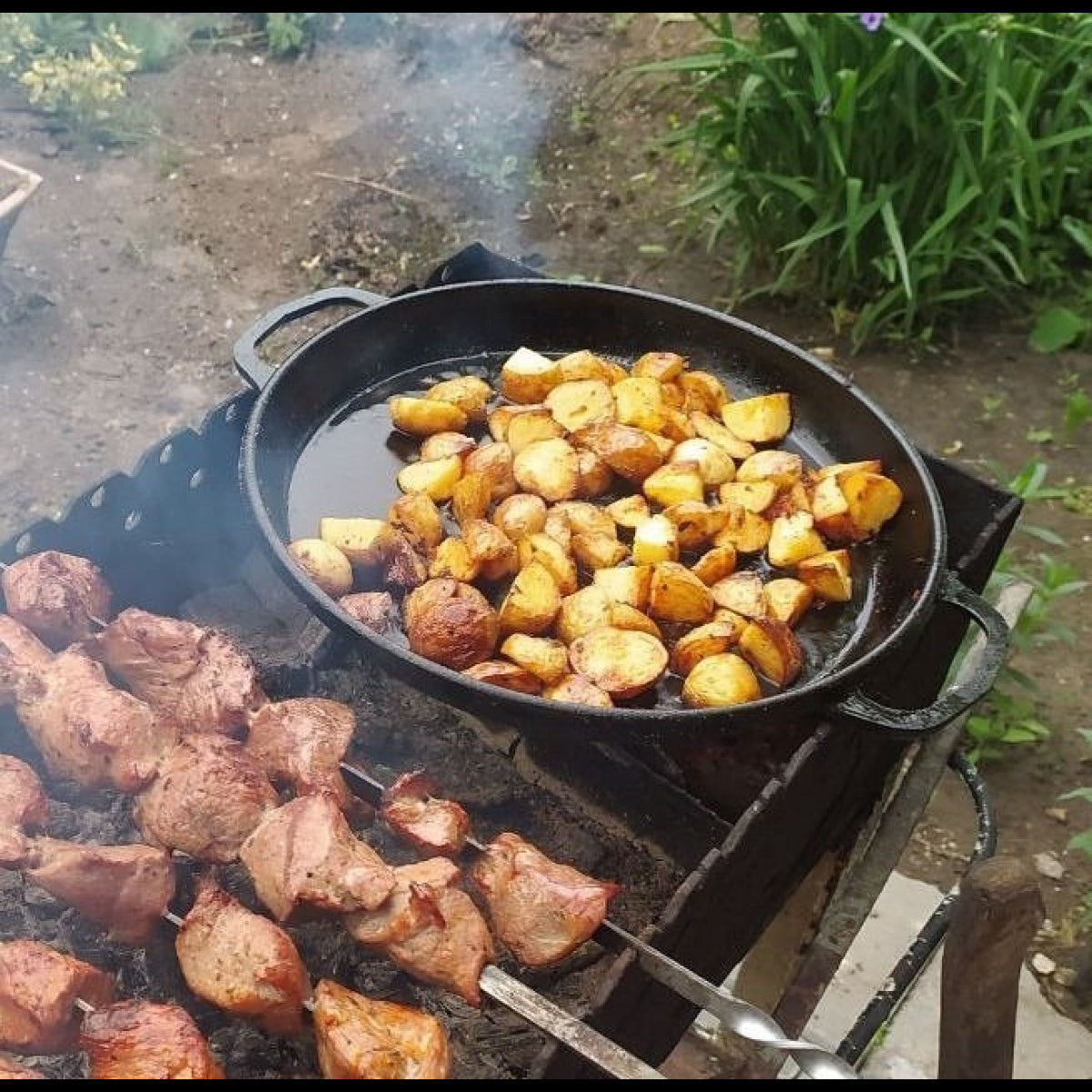 Skewers of meat and roasted potatoes cooking on a grill outdoors.