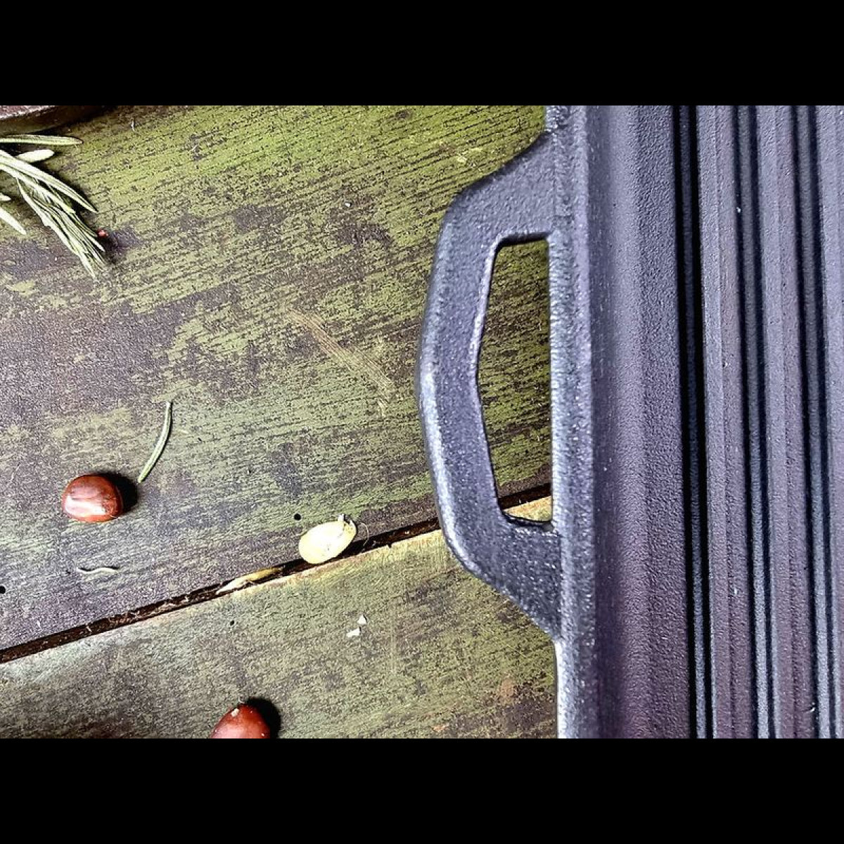Close-up of a cast iron skillet handle on a wooden surface with leaves and nuts.