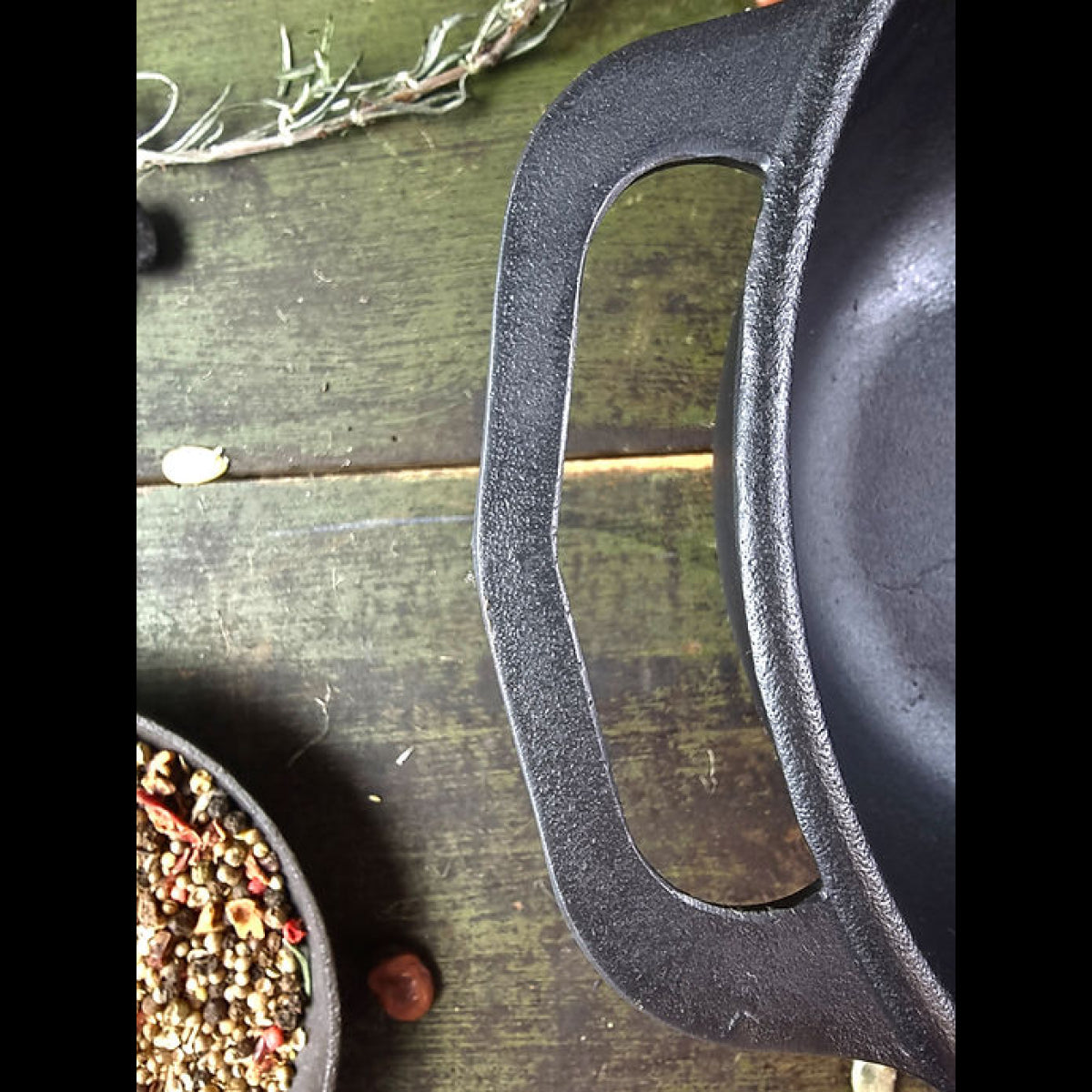 Close-up of a cast iron skillet handle on a wooden surface with herbs and spices.