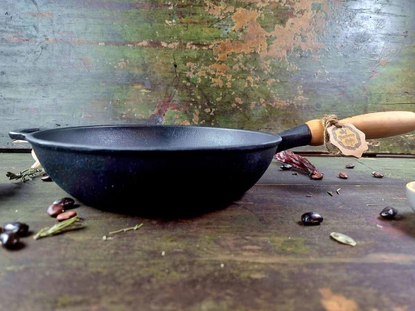 Black cast iron frying pan with wooden handle on a rustic wooden surface with spices.