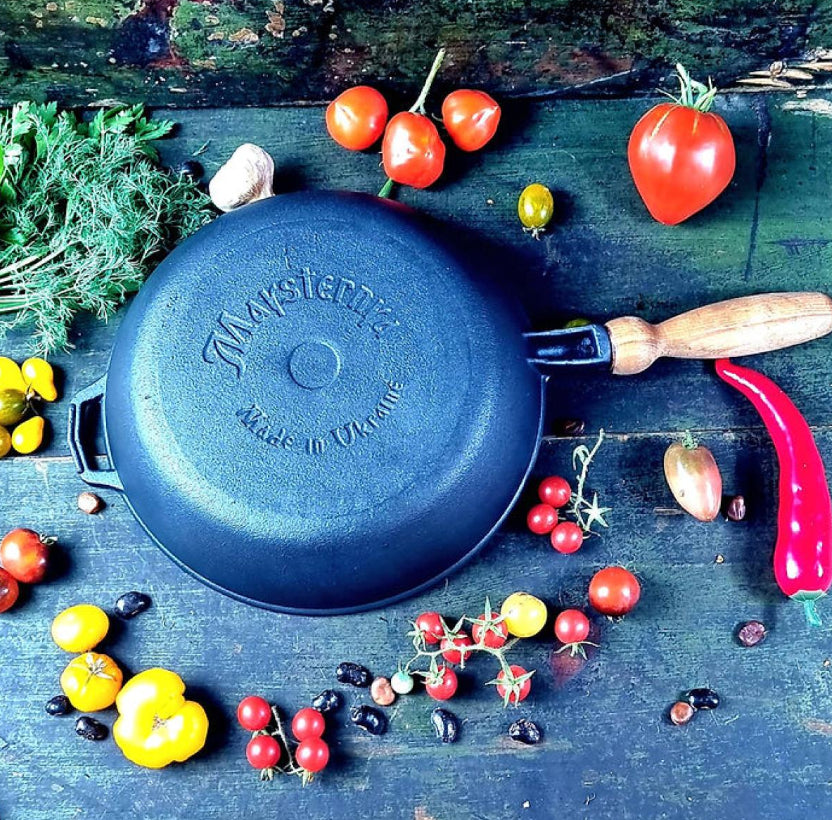 Black cast iron frying pan with wooden handle on a rustic wooden surface with vegetables